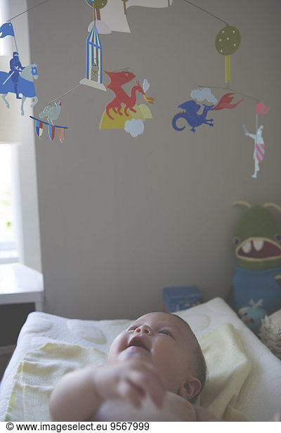 Little baby lying down and looking at colorful hanging mobile