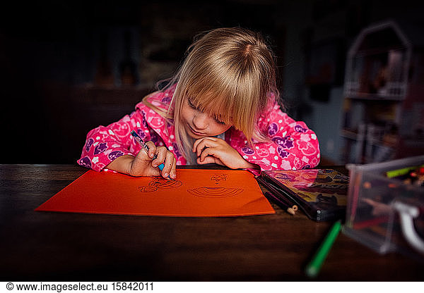 Little blond haired girl drawing a picture at a table on a sunny day