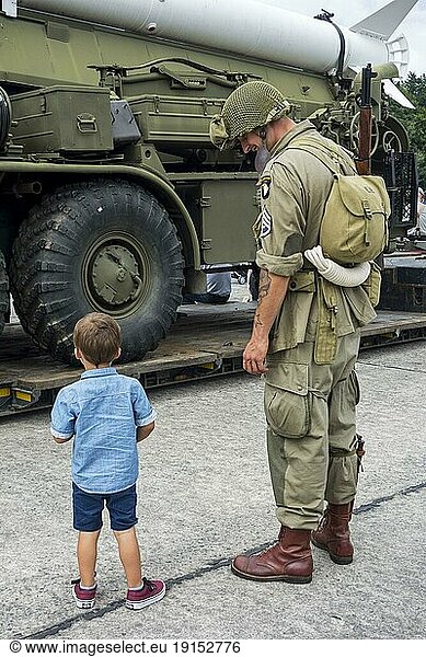 Little boy and WW2 reenactor in US soldier outfit looking at missile truck at World War Two militaria fair
