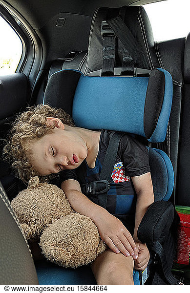 Little boy asleep in his car seat with his favorite stuffed toy