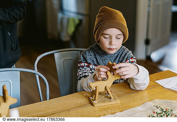 Little boy assembling gingerbread reindeer figurine on christmas