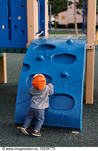 Little boy at the playground wearing a bright orange fox-design hat.