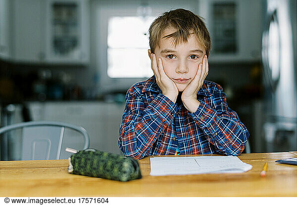 Little boy doing his homework and holding face in hands