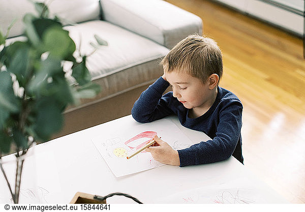 Little boy drawing at a living room table.