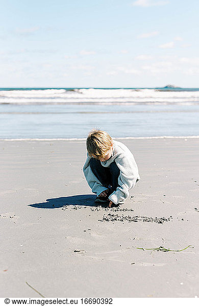 Little boy drawing in the sand on a beach in Massachusetts