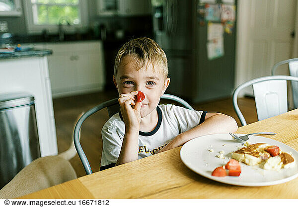 Little boy eating a pancake with fresh strawberries at home