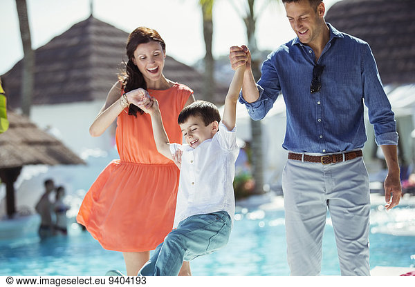 Little boy having fun with his parents by swimming pool