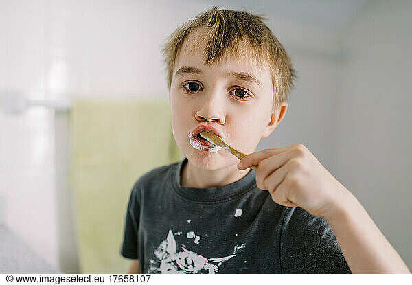 Little boy in bathroom brushing his teeth with wooden toothbrush