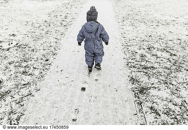 Little boy in blue onesie and warm hat walking on a snow