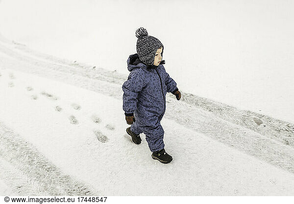 Little boy in blue onesie confidently walking outside on a snow