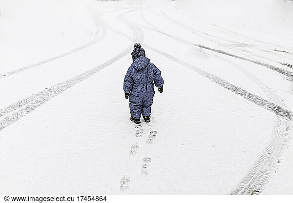 Little boy in blue onesie walking outside on a snow