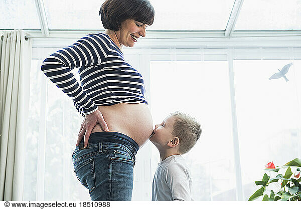 Little boy kissing a stomach of pregnant mother at home