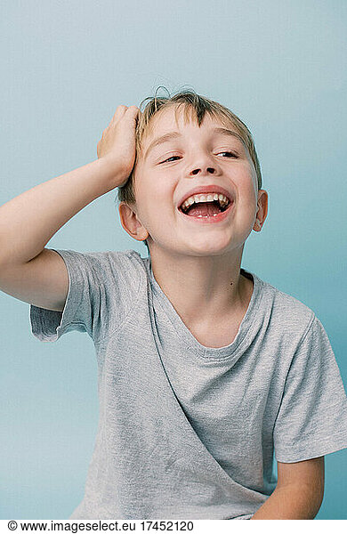 Little boy laughing and holding his head on blue background