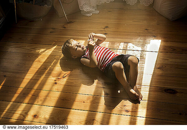 Little boy laying down on wooden floor in sunrays