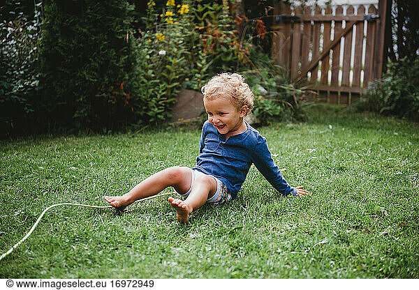 Little boy playing in baykyard in summer having fun sitting on grass