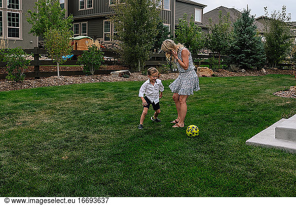 Little boy playing soccer with his mom in the yard
