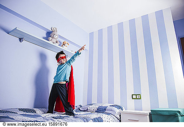 Little boy playing super hero  standing on his bed