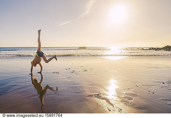 Little boy practicing handstand on the beach