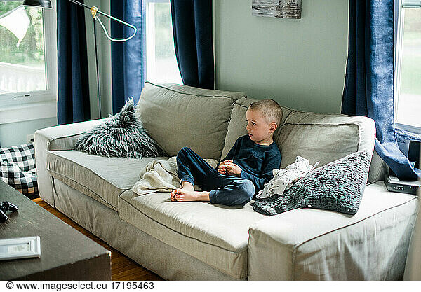 Little boy relaxing on sofa watching television in sweatpants alone
