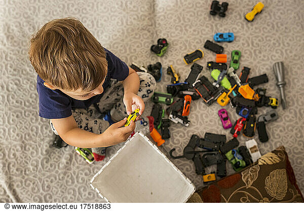 Little boy sitting on bed playing with toy cars