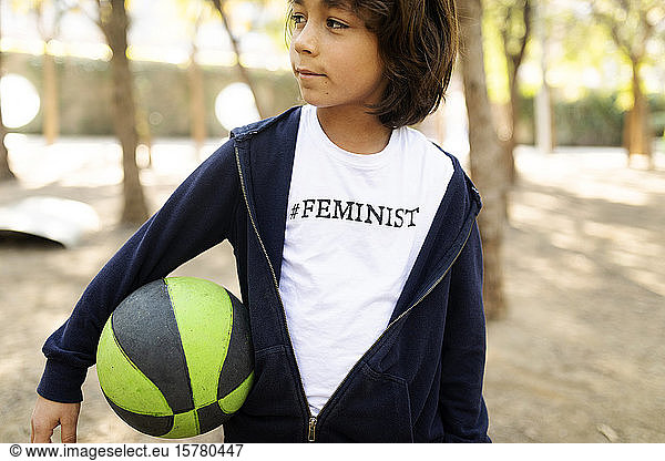 Little boy standing in the street with print on t-shirt  saying Feminist  holding ball