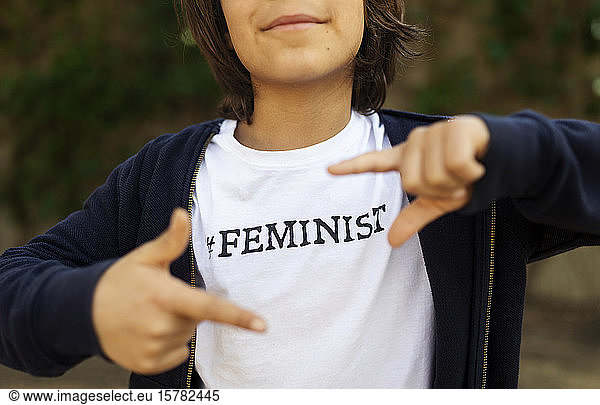 Little boy standing in the street with print on t-shirt  saying Feminist  making finger frame