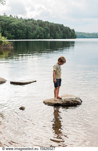 Little boy standing on a rock surrounded by water.