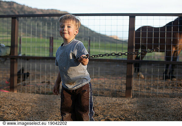 Little boy swinging chain with horse in background