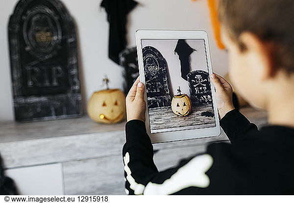 Little boy taking photo of Halloween decoration with digital tablet