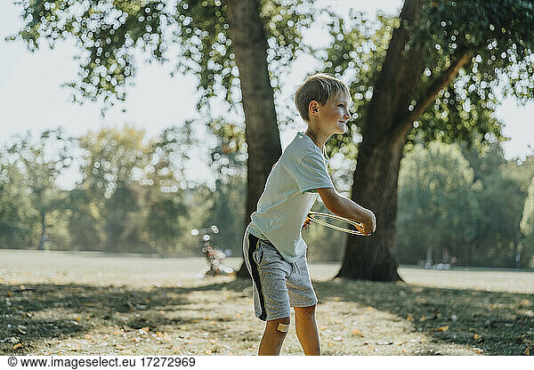 Little boy throwing frisbee ring while standing in public park on sunny day