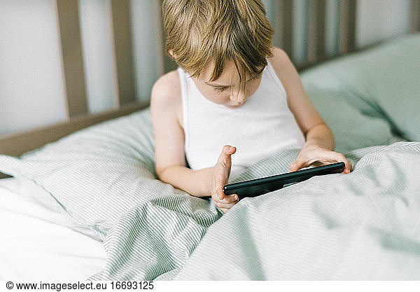 Little boy waking up in the morning playing his tablet
