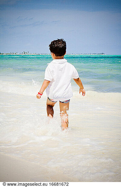 Little boy walking on the beach watching the Caribbean ocean