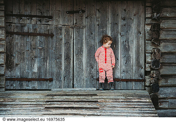Little boy wearing Scandinavian onesie outside wooden old house winter