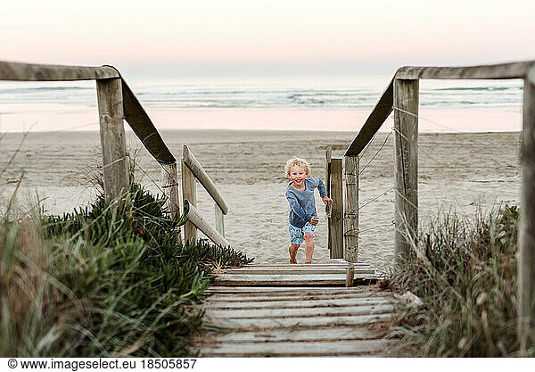 Little boy with curly hair on wooden path at beach