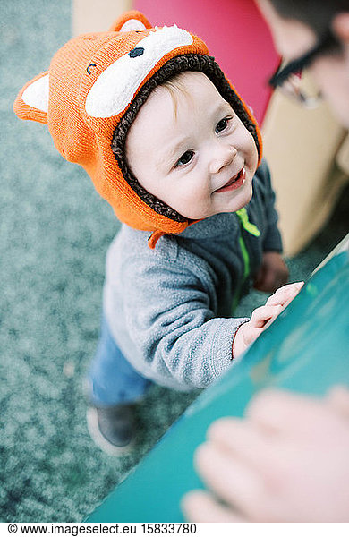 Little boy with fox hat at the playground smiling at his father.