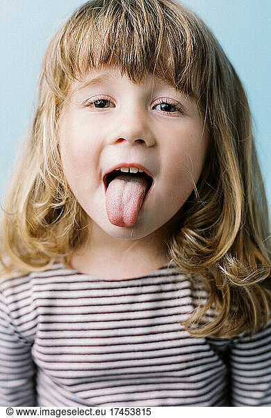 Little cheeky toddler girl with messy hair sticking out her tongue