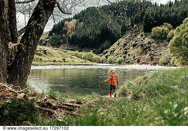 Little curly haired kid exploring river bank in boots