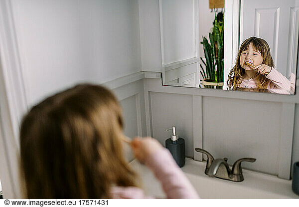 Little girl brushing her teeth independently in the bathroom
