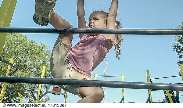 Little girl climbs gymnastic ladder on open sports ground on outside. Cute little girl crawls on vertical sports ladder in city park on sun day. Odessa  Ukraine  Europe