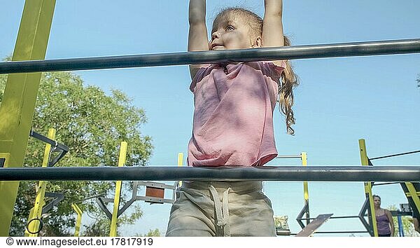 Little girl climbs gymnastic ladder on open sports ground on outside. Cute little girl crawls on vertical sports ladder in city park on sun day. Odessa  Ukraine  Europe