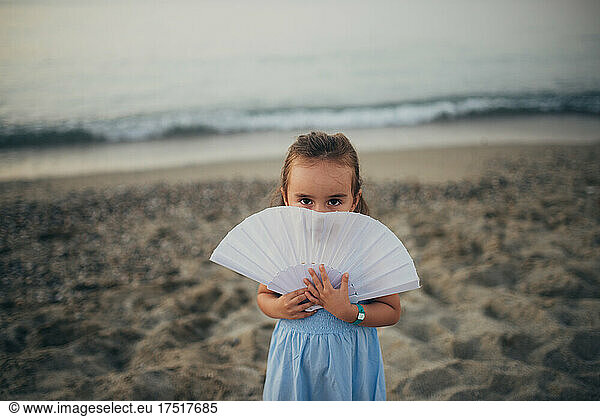 Little girl cover face with fan on the beach.