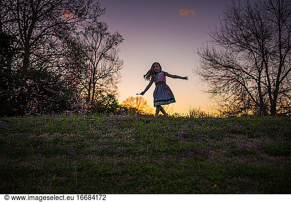 Little girl dancing sunset grass flowers silohette hill trees twirling