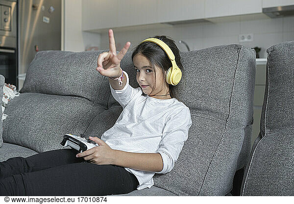 Little girl doing peace sign while playing video game in living room