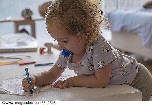 Little girl drawing with colors in the room of the house.