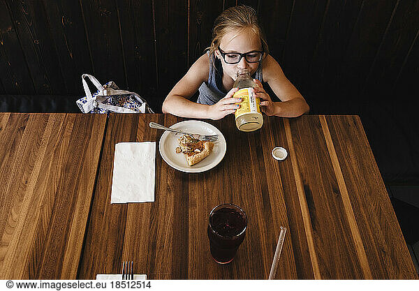 Little girl eats and drinks at table in cafe restaurant