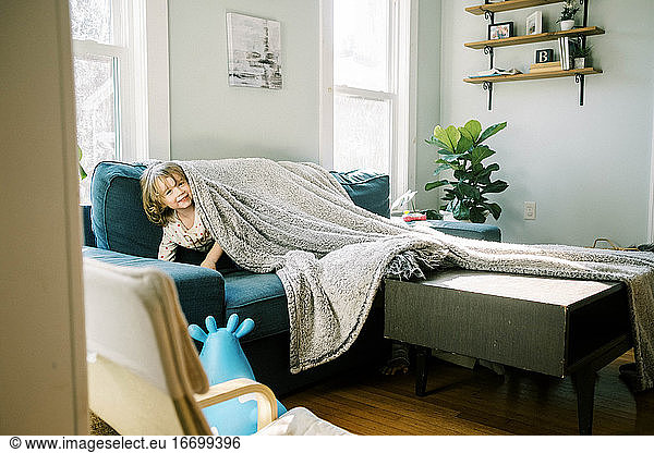 Little girl hiding under a blanket in the living room