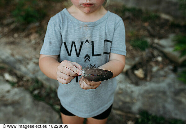 Little girl holding a bird feather on a hike