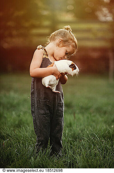 little girl holding her pet guinea pig outside