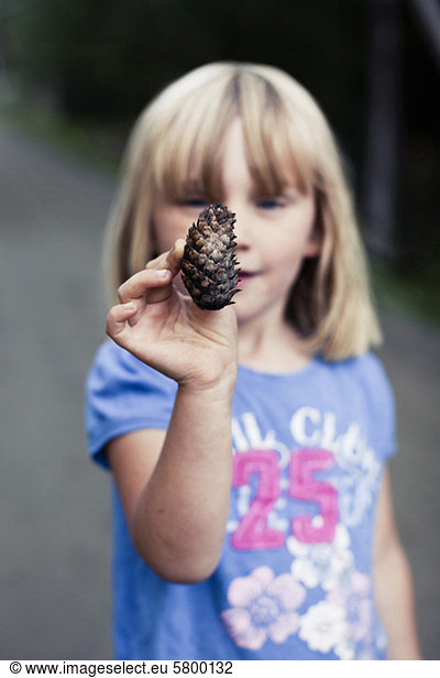 Little girl holding up a pine cone
