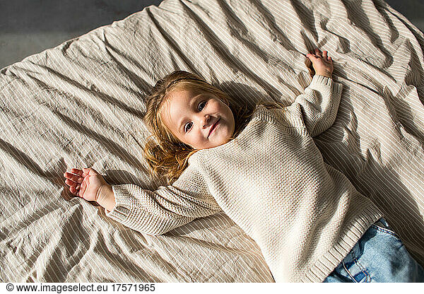 Little girl in cozy white sweater lying in bed